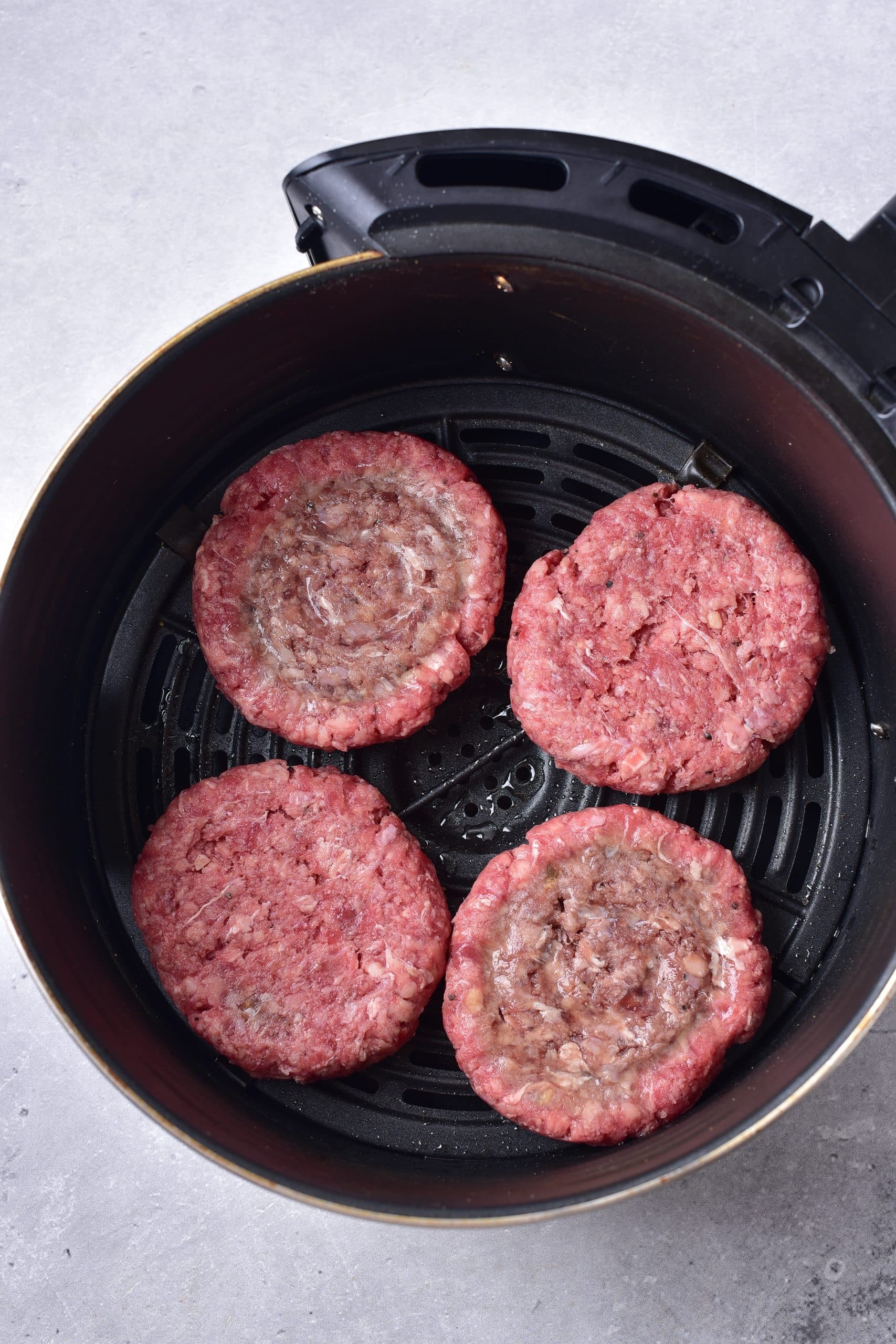 four raw hamburger patties in the basket of an air fryer