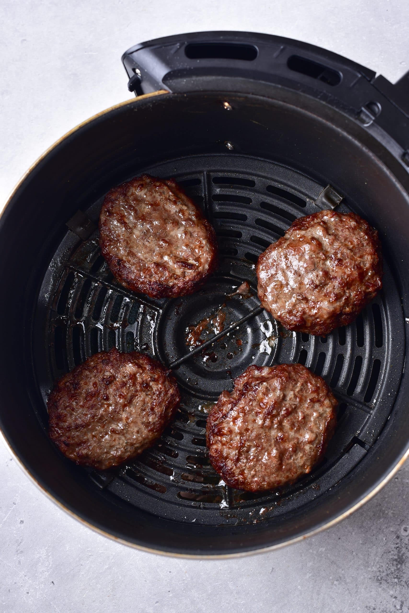 cooked hamburger patties in the basket of an air fryer