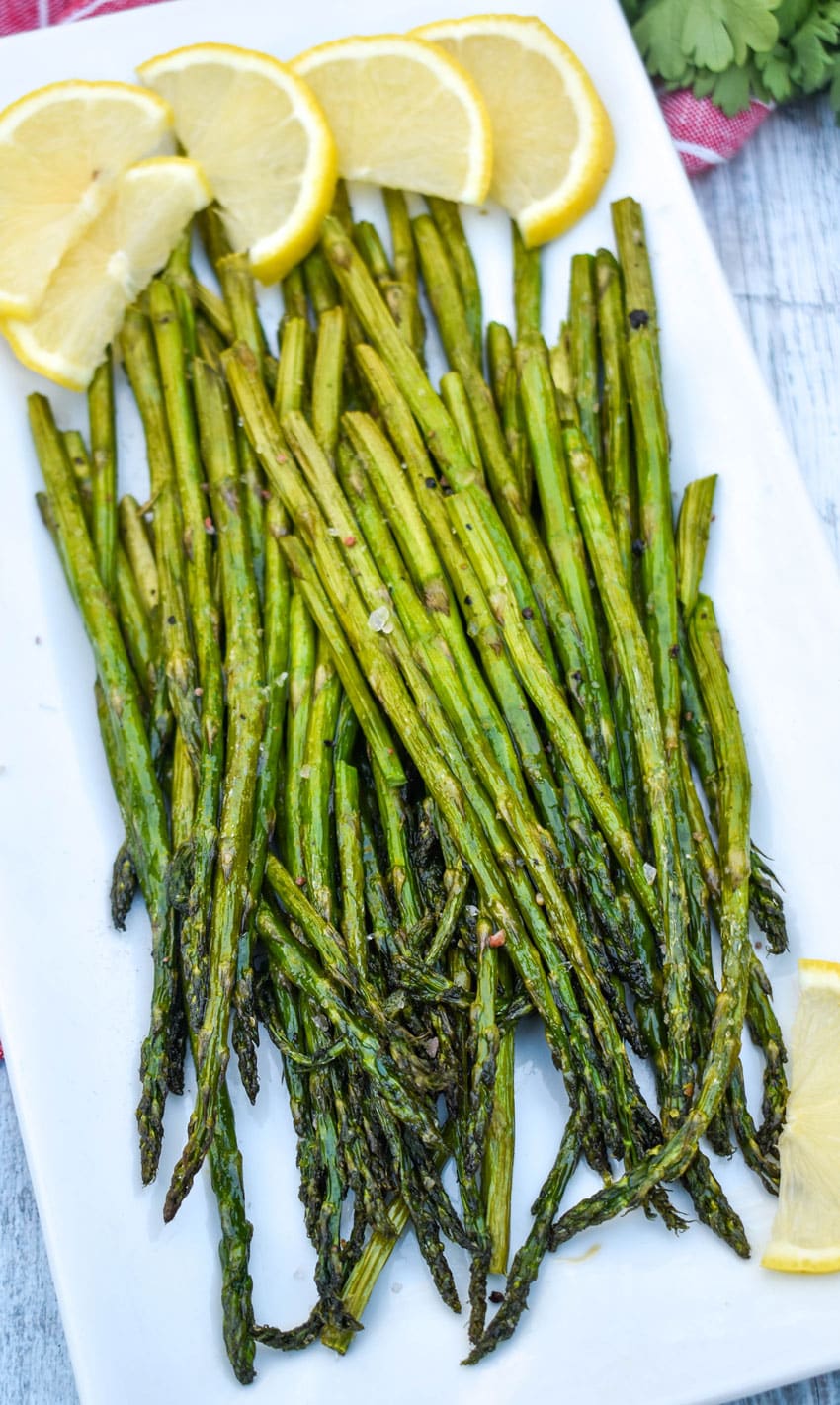 stalks of air fryer roasted asparagus on a white serving platter with slices of lemon on the side