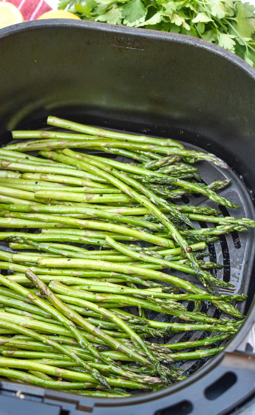 stalks of asparagus coated in olive oil and seasoned with salt and pepper arranged in the basket of an air fryer