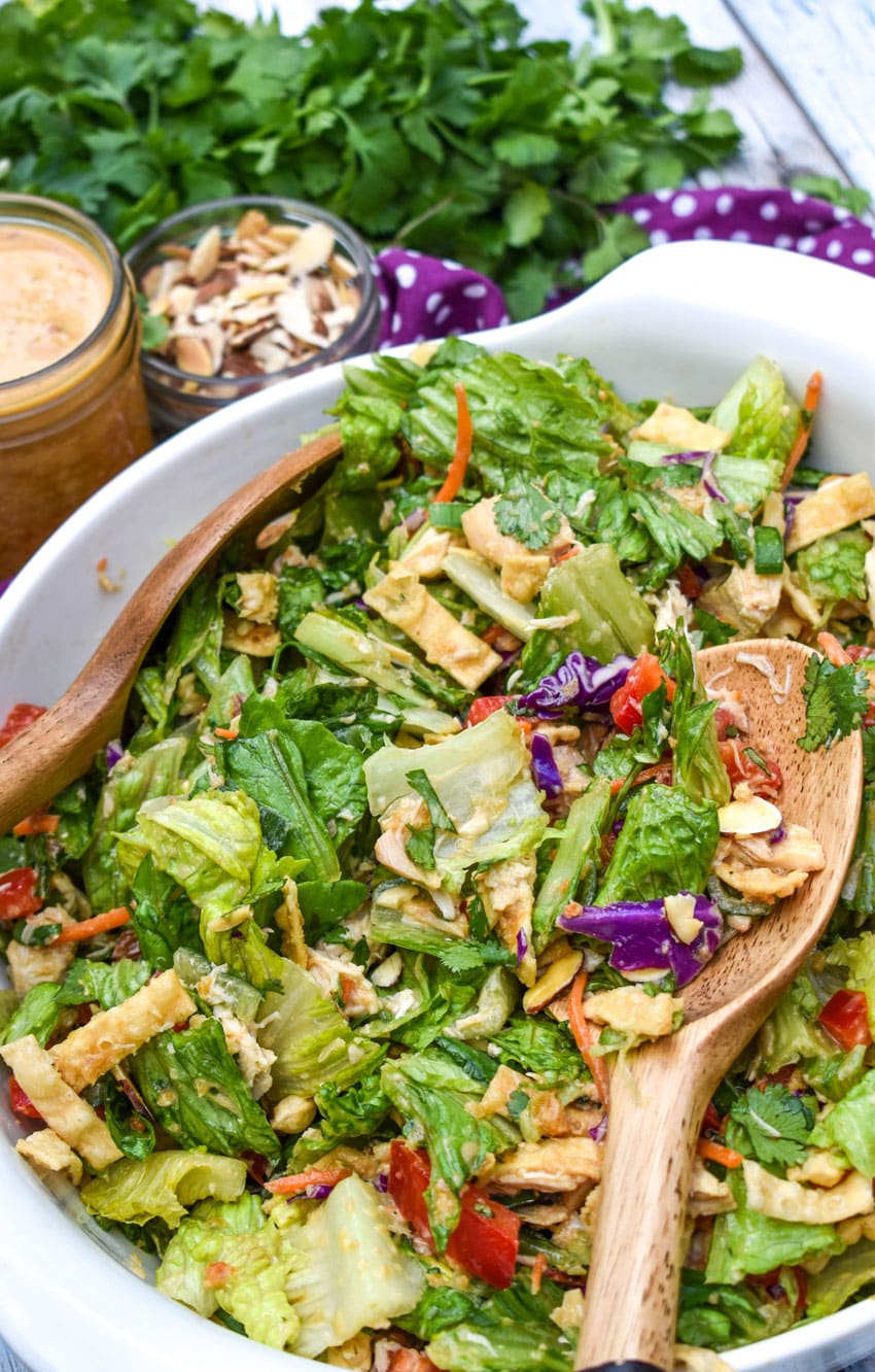two wooden salad servers digging into an asian chopped salad in a white bowl