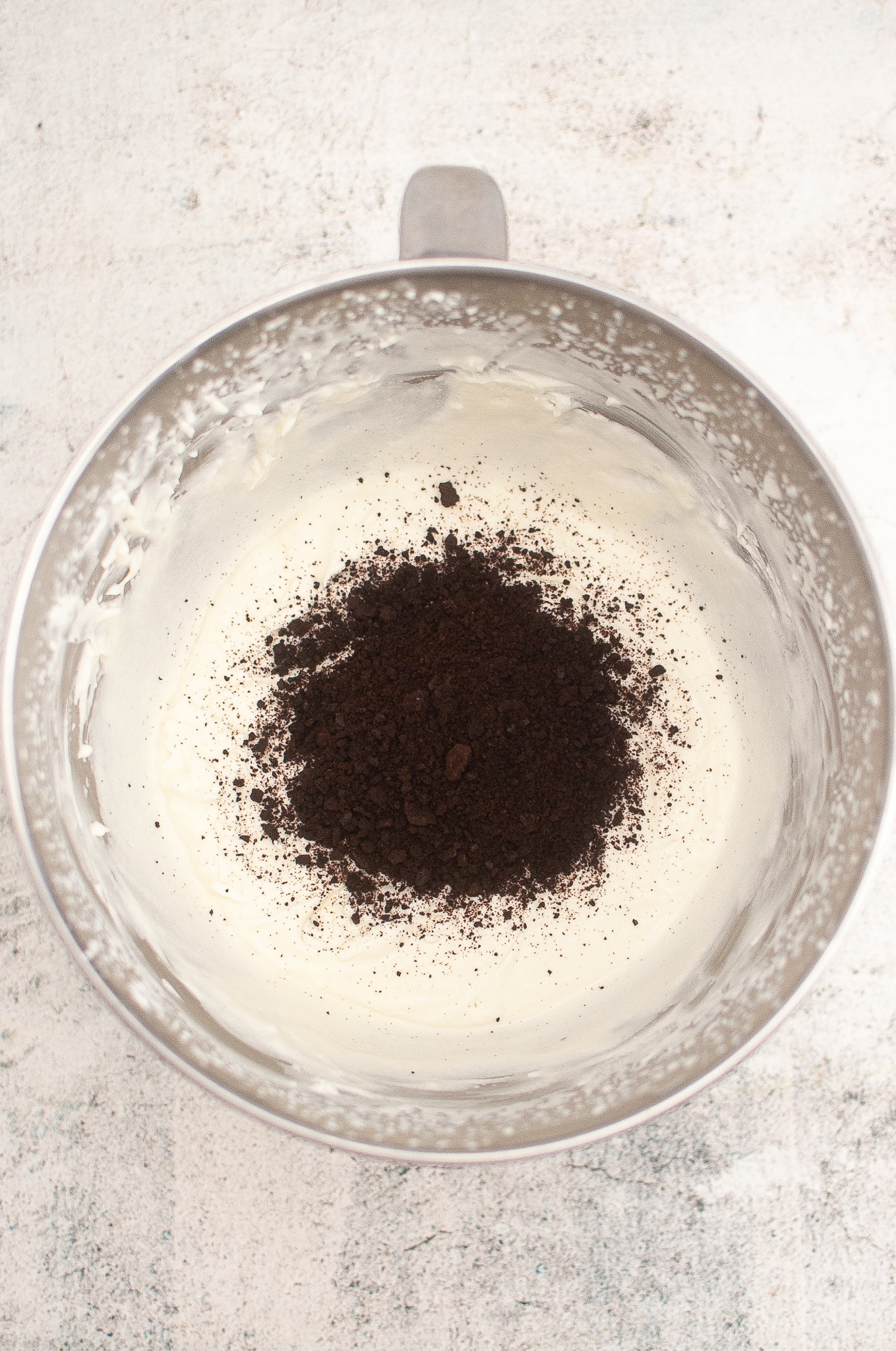oreo cookie crumbs sitting on whipped cream in a metal mixing bowl