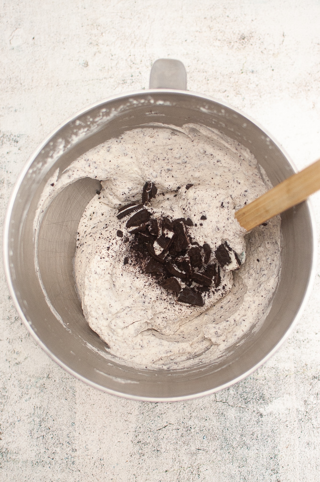 oreo cookies in whipped cream being stirred together by a spatula in a metal mixing bowl