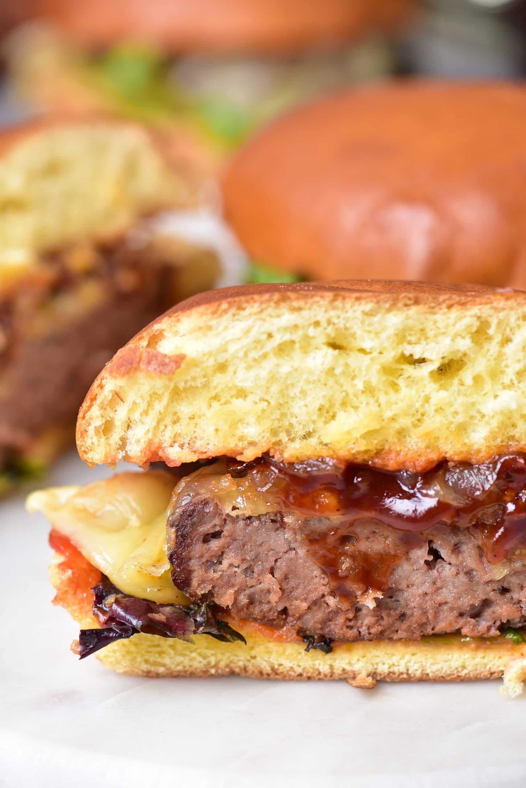 a close up image showing an air fryer burger cut in half with barbecue sauce oozing out the center on a marble cutting board