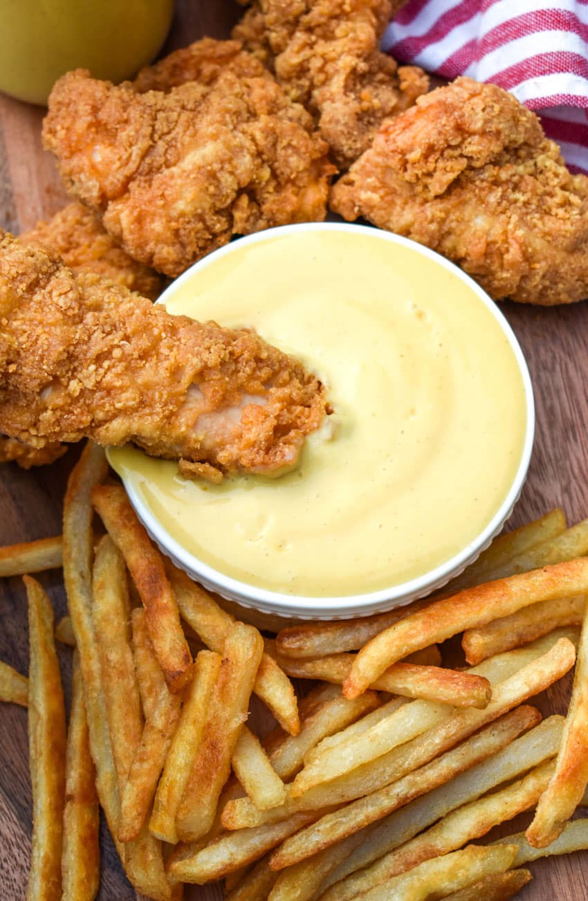a chicken tender being dipping in homemade honey mustard sauce in a small white dipping bowl