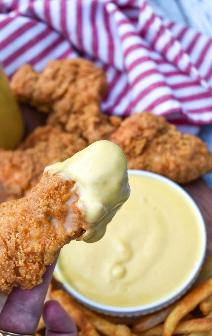 a hand holding up a chicken tender that's been dipped in homemade honey mustard sauce