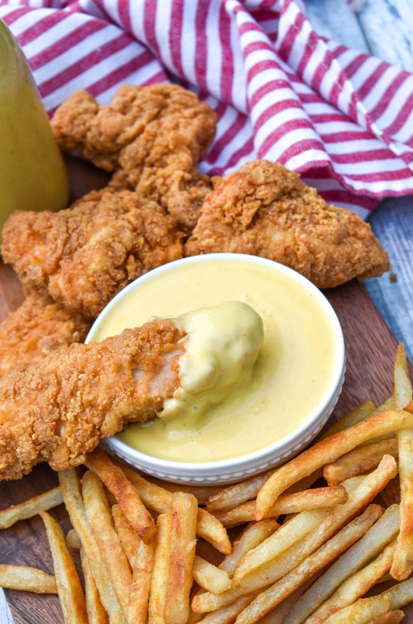a chicken tender being dipped in homemade honey mustard sauce in a small white dipping bowl