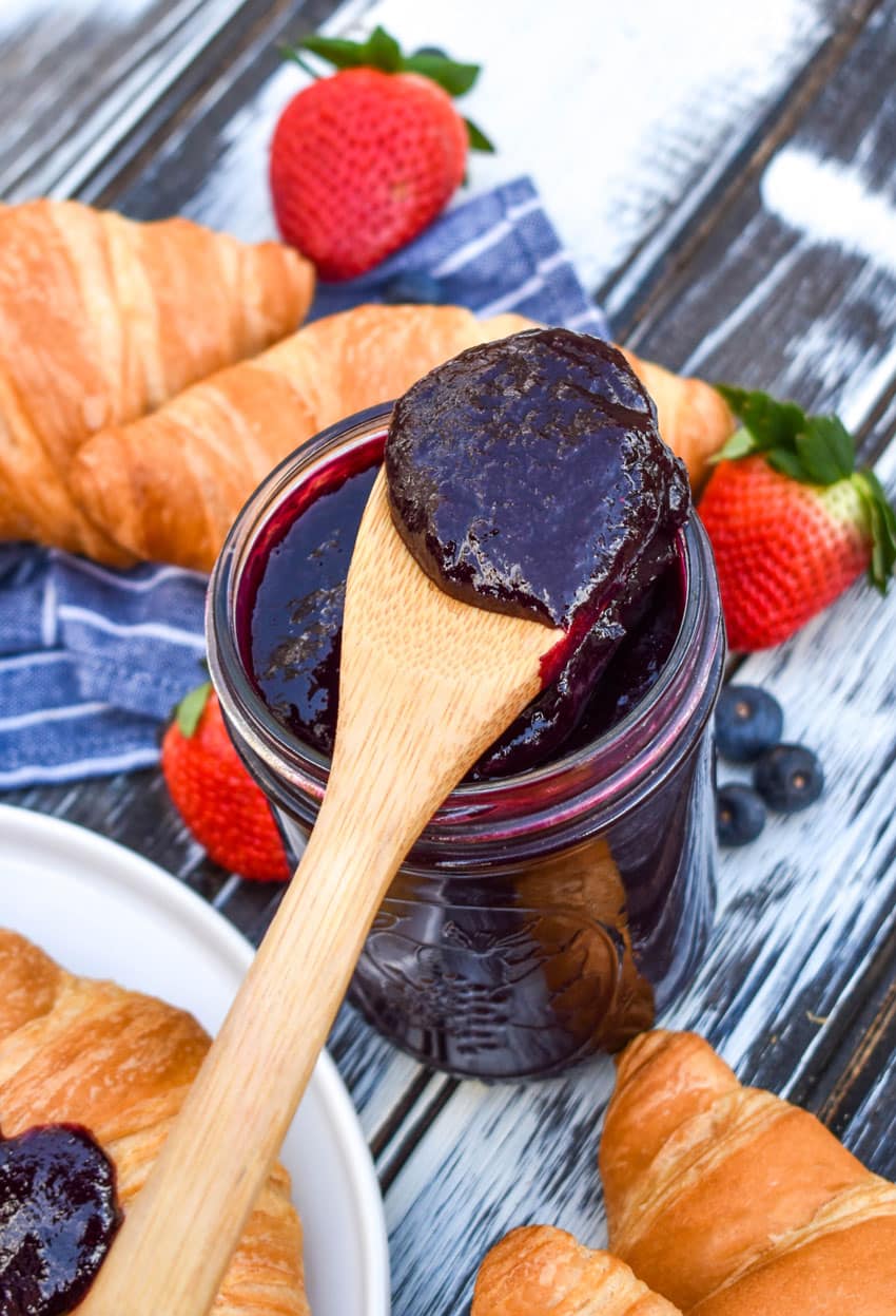 a wooden spoon resting on the edge of a glass jar holding a scoop of crockpot blueberry sauce