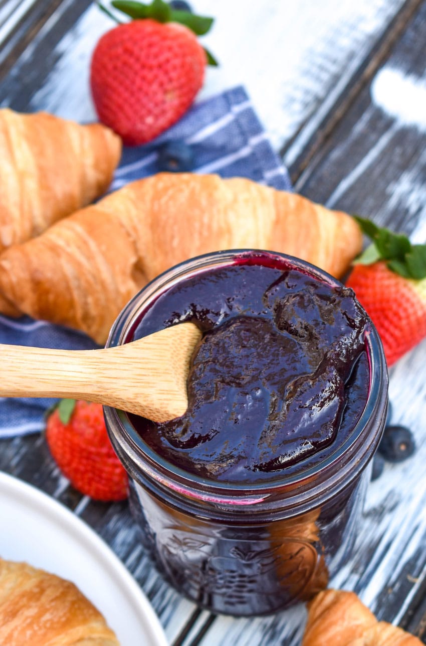 a wooden spoon in a glass jar filled with slow cooker blueberry butter