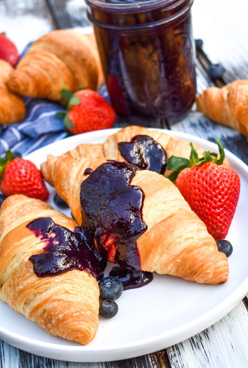 crockpot blueberry sauce spread over two croissants on a white plate with fresh fruit on the side