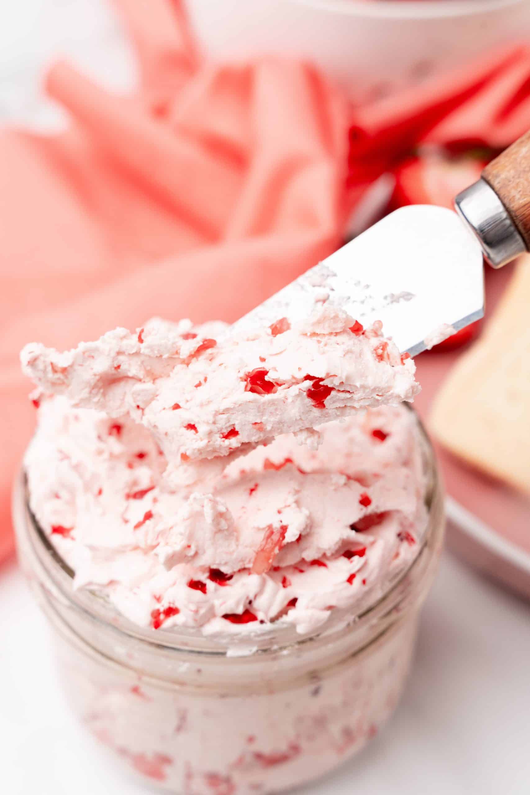 a metal butter knife scooping whipped strawberry butter out of a small glass jar