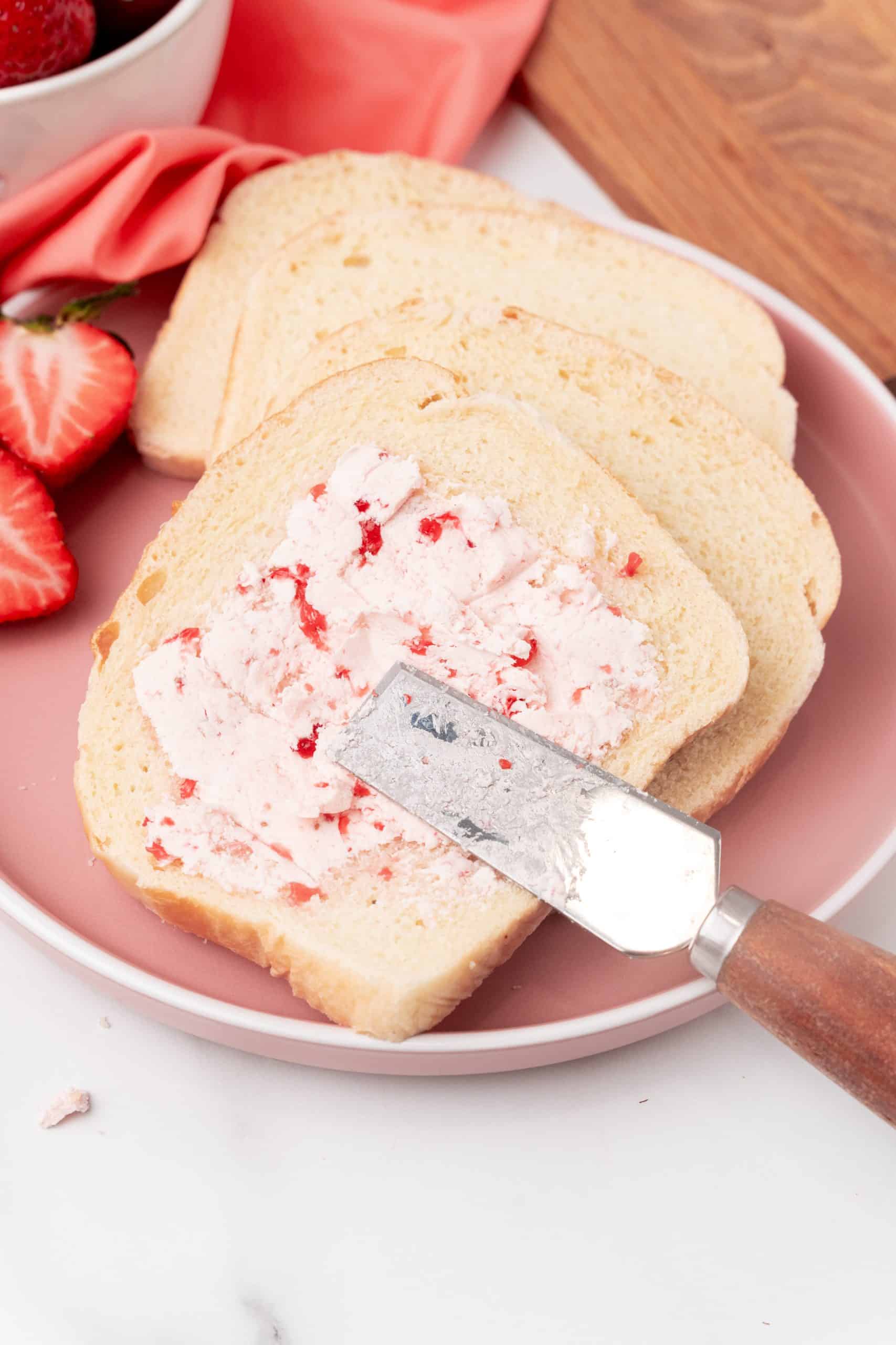 a metal spreader spreading whipped strawberry butter onto a slice of white bread