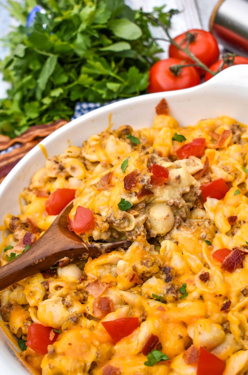 a wooden spoon scooping cheeseburger mac and cheese out of a white serving bowl