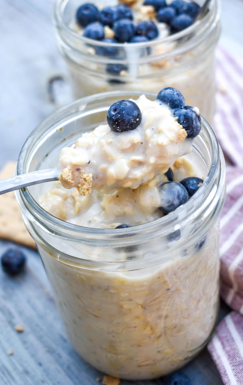 a silver spoon scooping blueberry overnight oats out of a glass jar