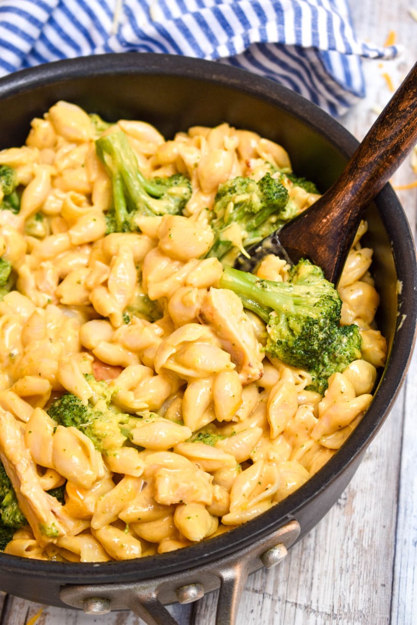 a wooden spoon scooping chicken and broccoli mac and cheese out of a black pot