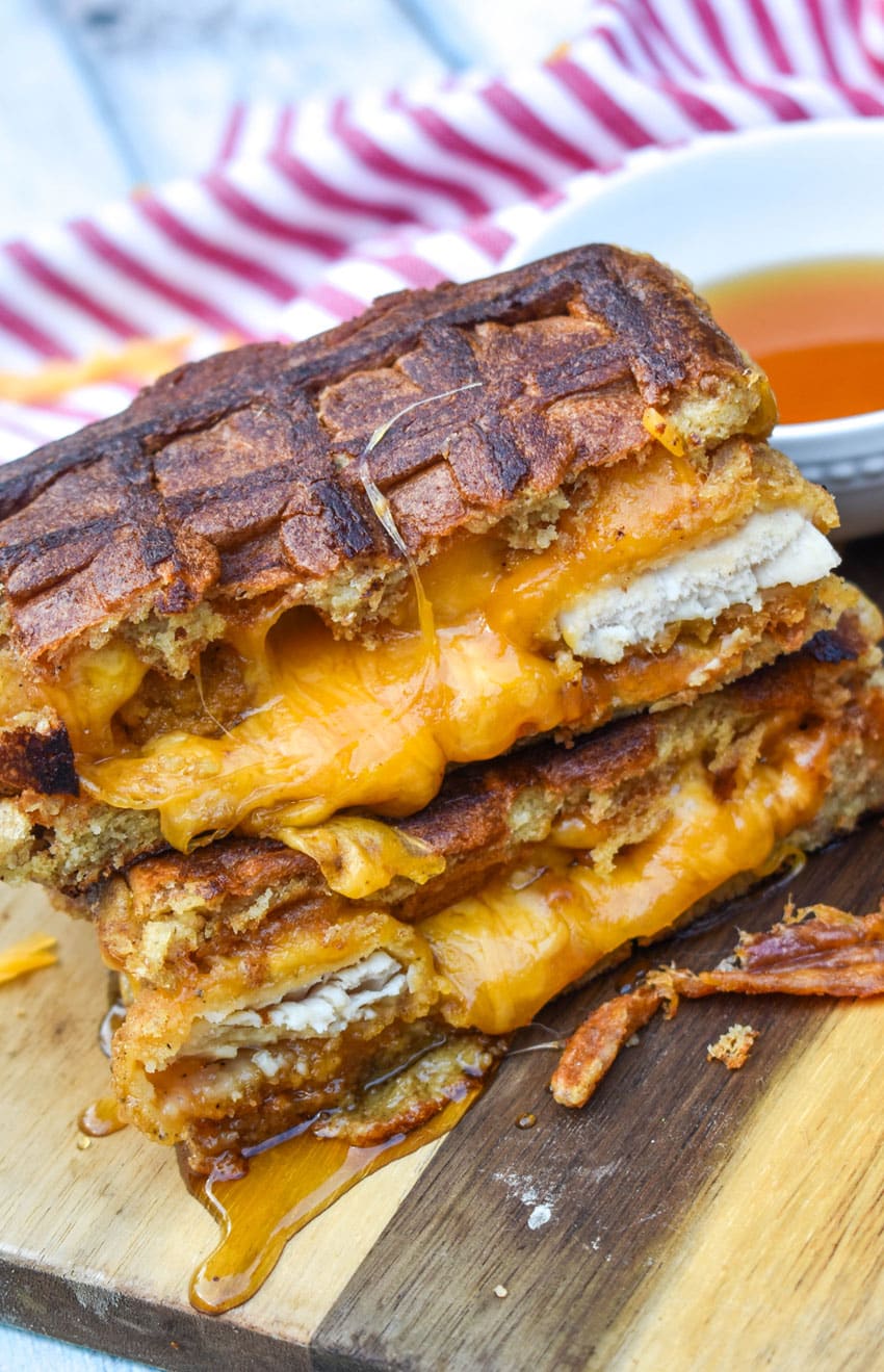 chicken and waffle grilled cheese sandwiches stacked on a wooden cutting board