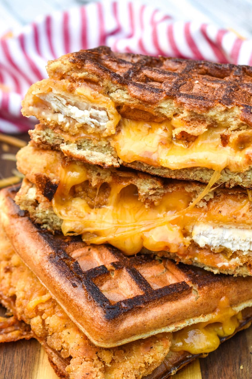 chicken and waffle grilled cheese sandwiches stacked on a wooden cutting board