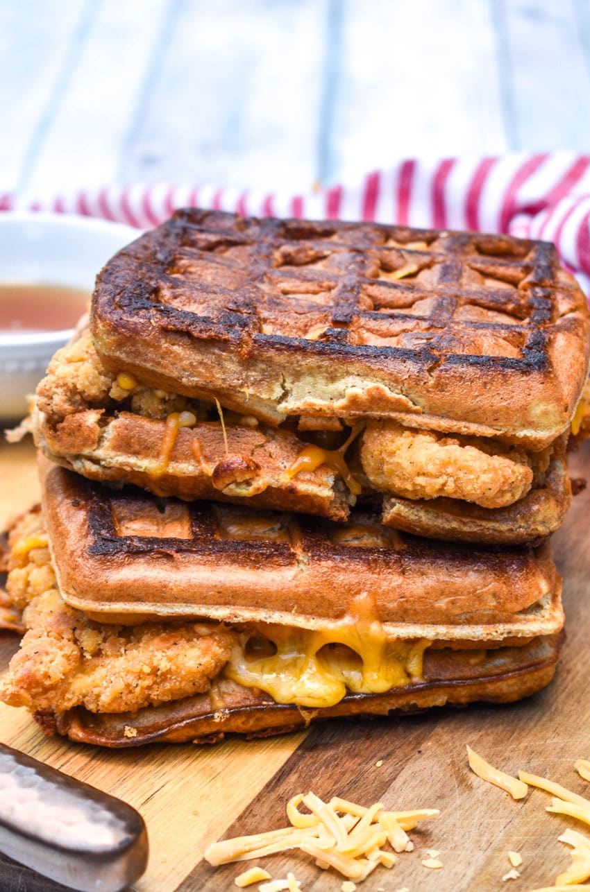 chicken and waffle grilled cheese sandwiches stacked on a wooden cutting board