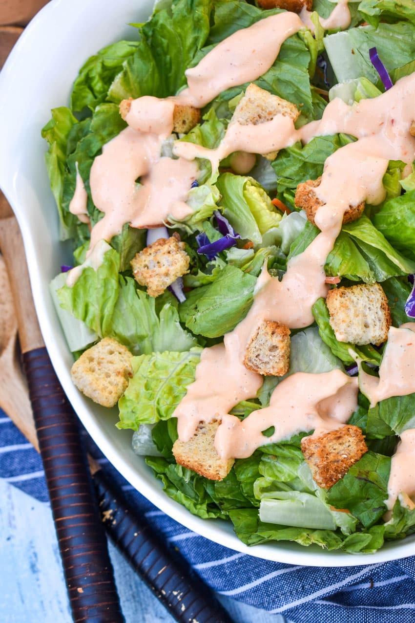homemade thousand island dressing drizzle over chopped lettuce in a white serving bowl