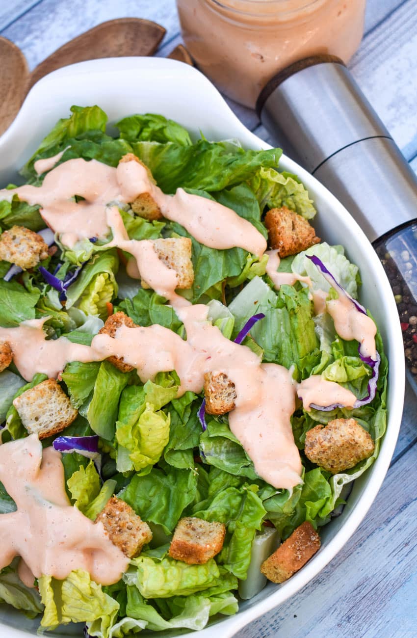 homemade thousand island dressing drizzle over chopped lettuce in a white serving bowl