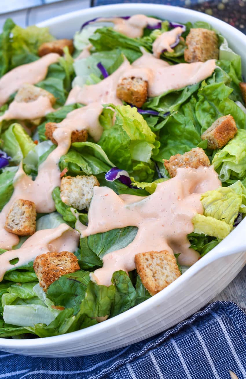 homemade thousand island dressing drizzle over chopped lettuce in a white serving bowl