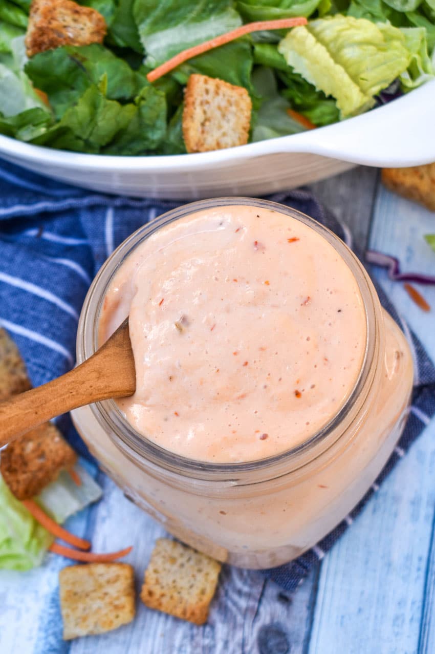 a wooden spoon scooping thousand island dressing out of a glass jar