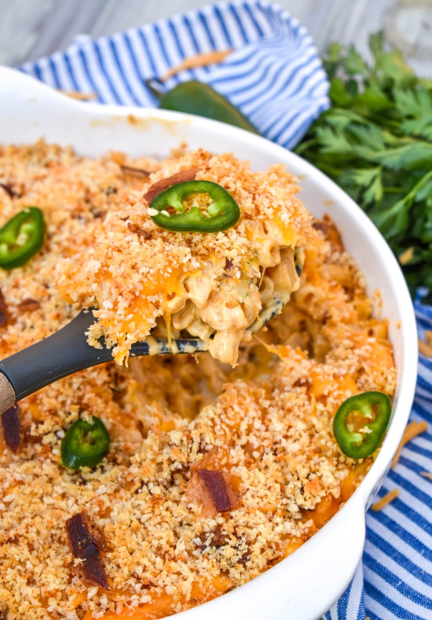 a serving spoon scooping jalapeno popper mac and cheese out of a large white serving bowl