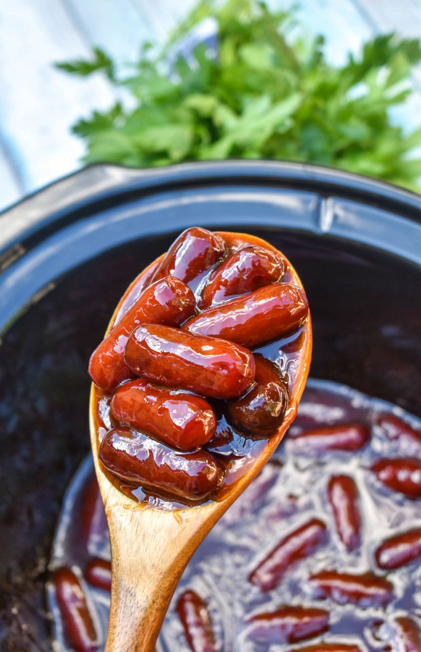 a wooden spoon holding up a scoop of slow cooker little smokies