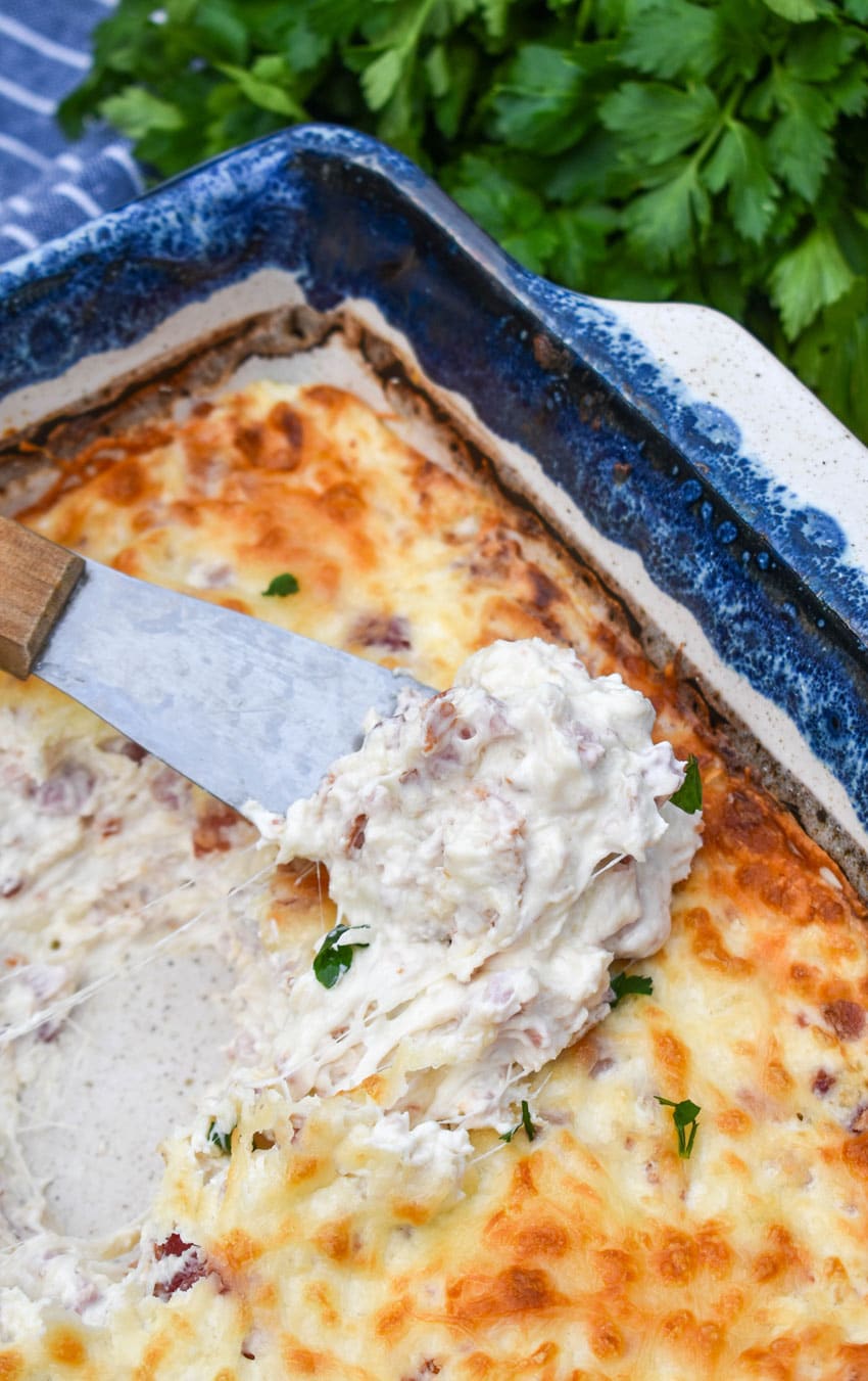 a cheese spreader scooping creamy chicken cordon bleu out of a baking dish