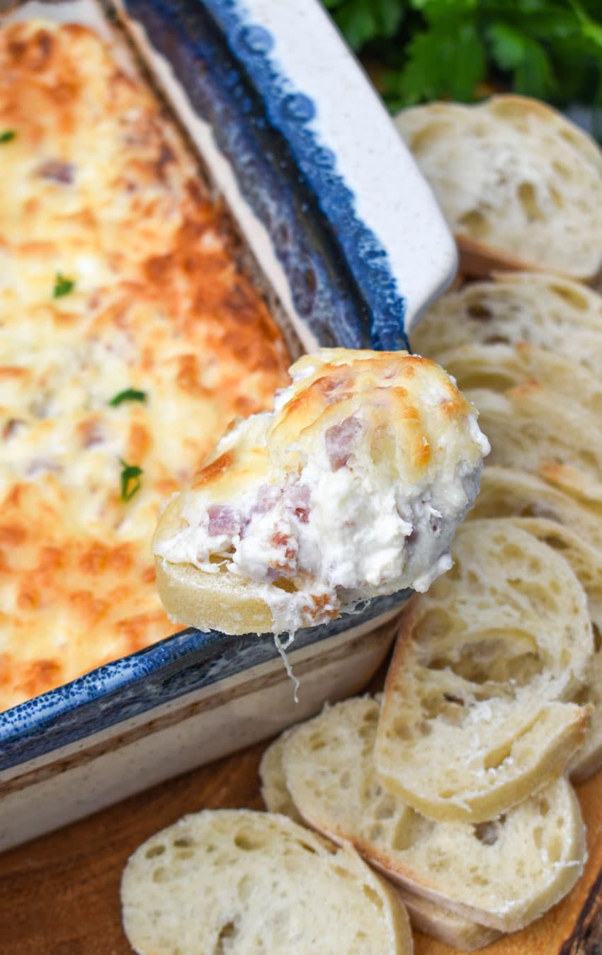 a chicken cordon bleu dip topped baguette slice resting on the corner of a square baking dish