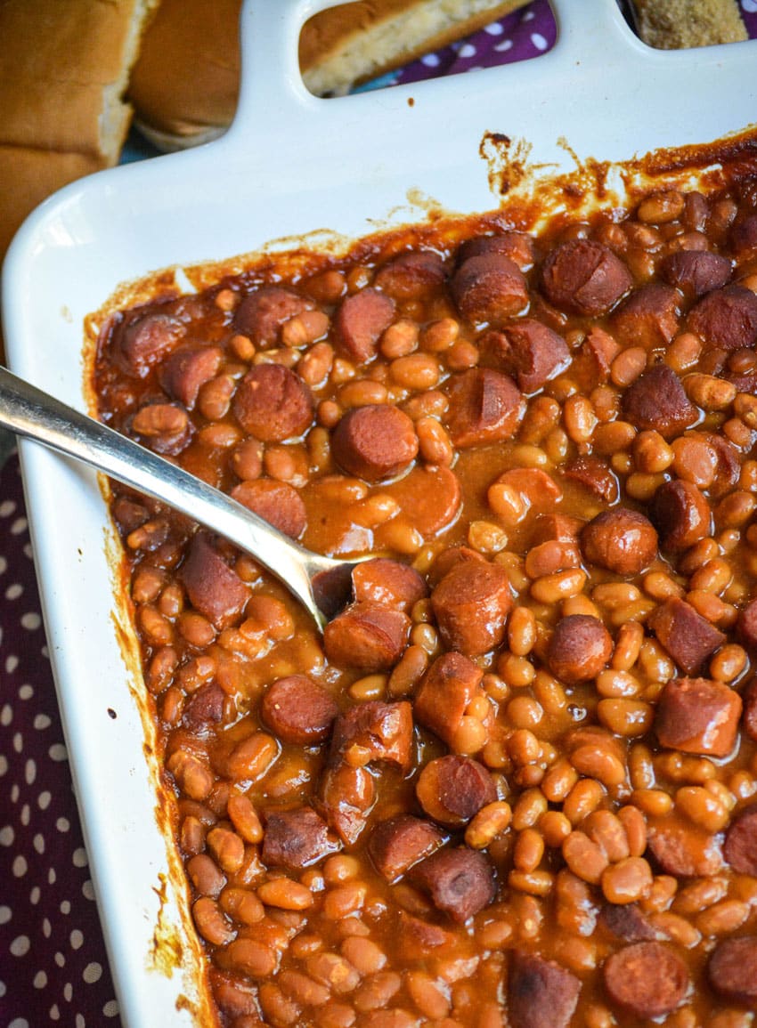 a silver spoon scooping frank and beans casserole out of a white baking dish