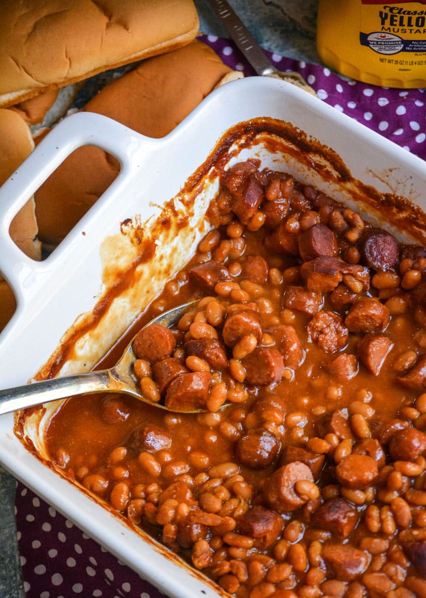 a silver spoon scooping frank and beans casserole out of a white baking dish