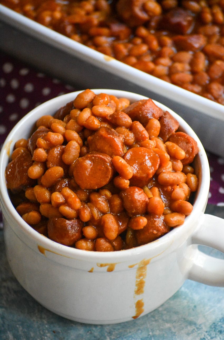 hotdogs and beans casserole in a white mug next to a white baking dish