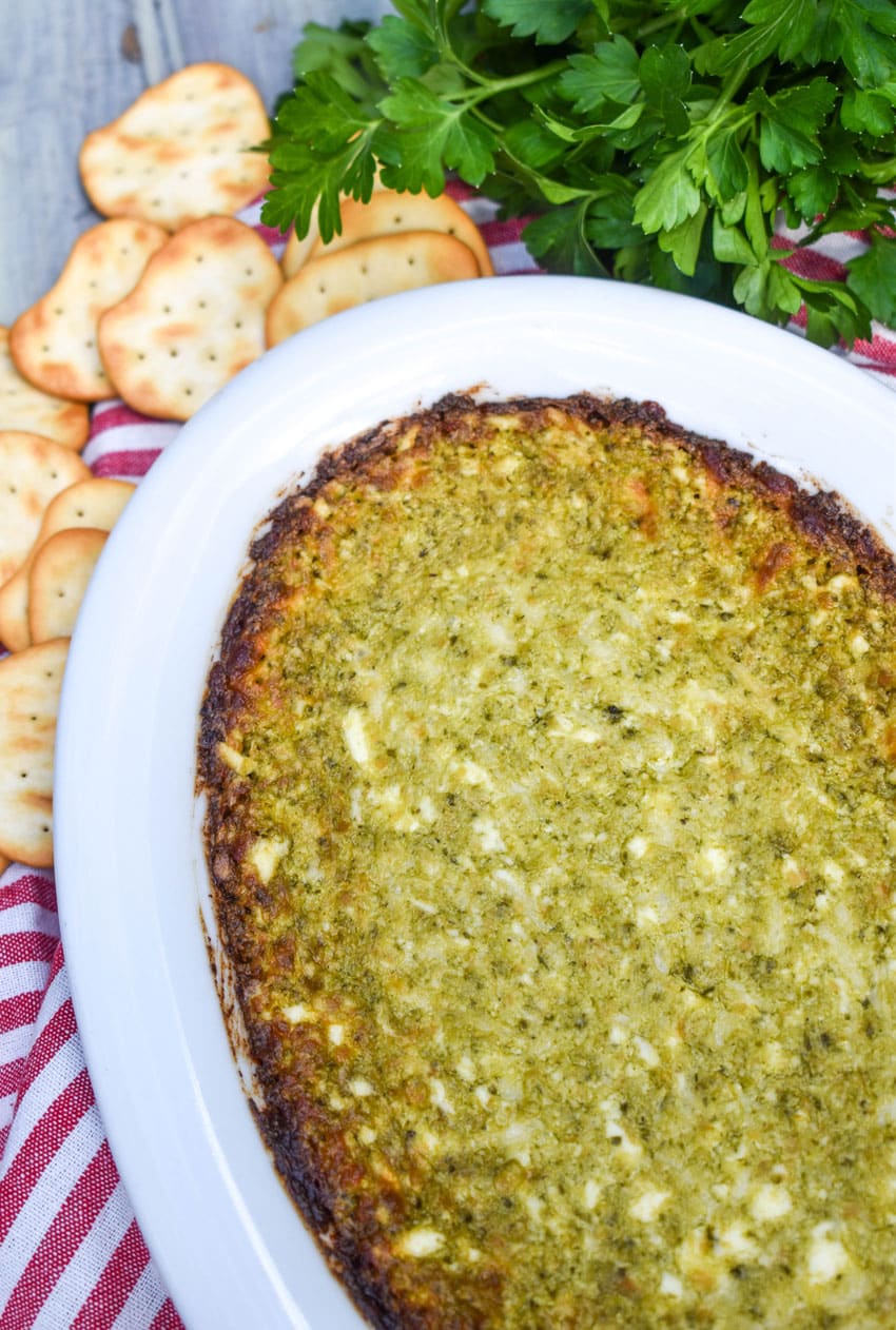 hot pesto dip in a white serving dish surrounded by crispy crackers