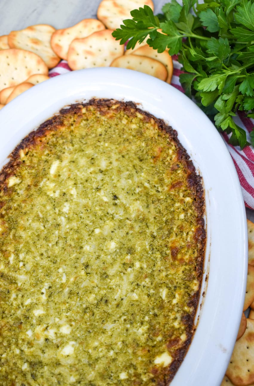 hot pesto dip in a white serving dish surrounded by crispy crackers