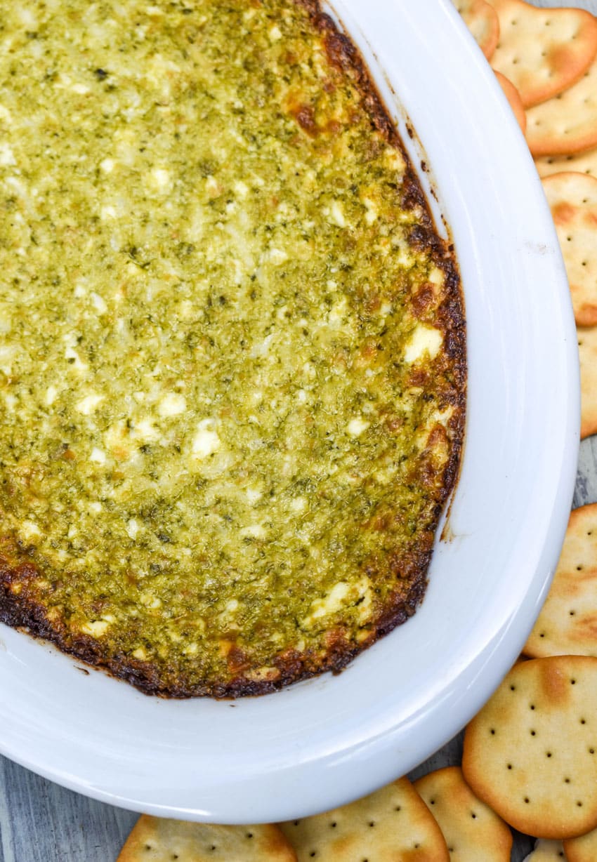 hot pesto dip in a white serving dish surrounded by crispy crackers