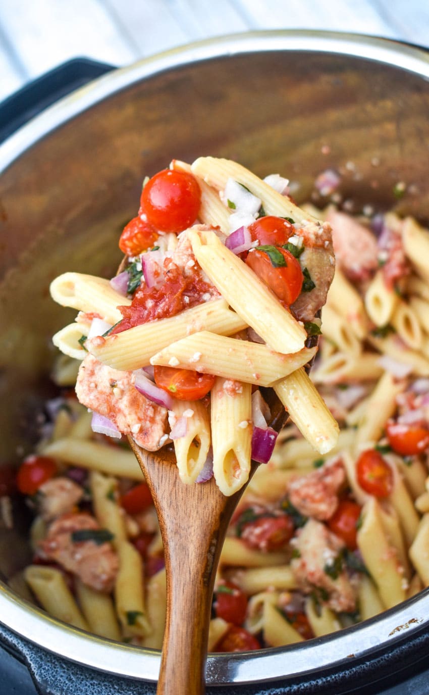 a wooden spoon holding up a scoop of instant pot bruschetta chicken and pasta