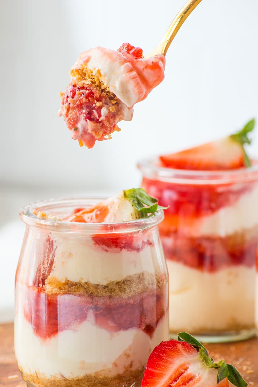a close up image of a gold spoon holding up a scoop of layered strawberry cheesecake 