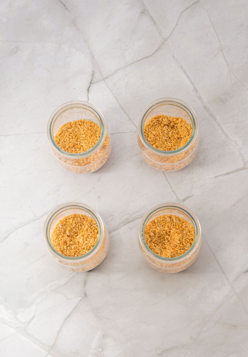 strawberry cheesecake layers being added to four small glass jars