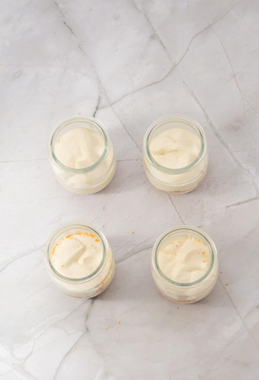 strawberry cheesecake layers being added to four small glass jars