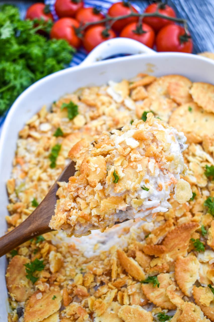 a wooden spoon lifting a scoop of shrimp and rice casserole out of a white baking dish