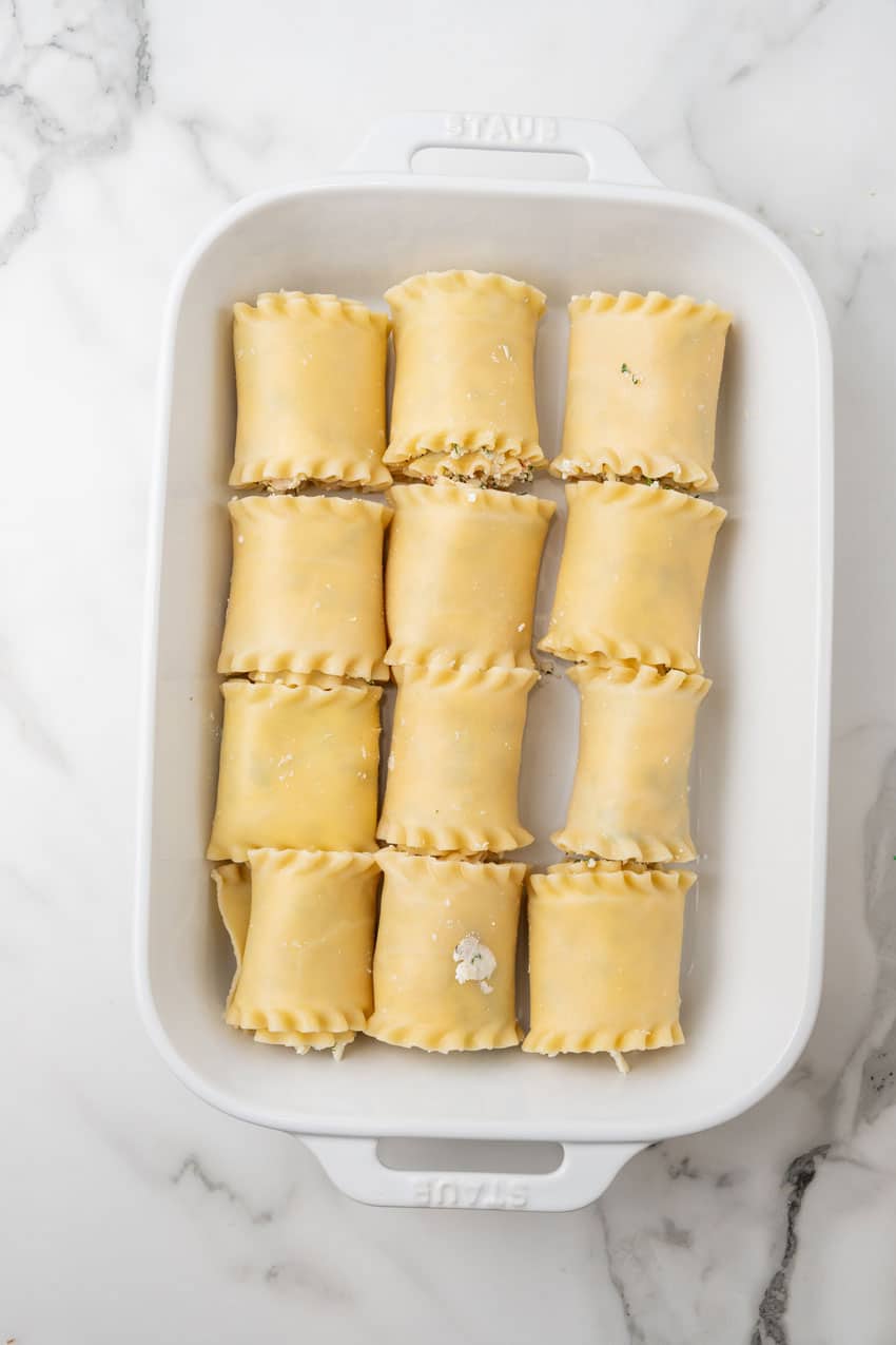 white chicken lasagna roll ups arranged in rows in a white baking dish