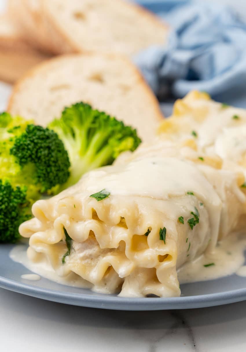 white chicken lasagna roll ups and steamed broccoli on a small blue plate