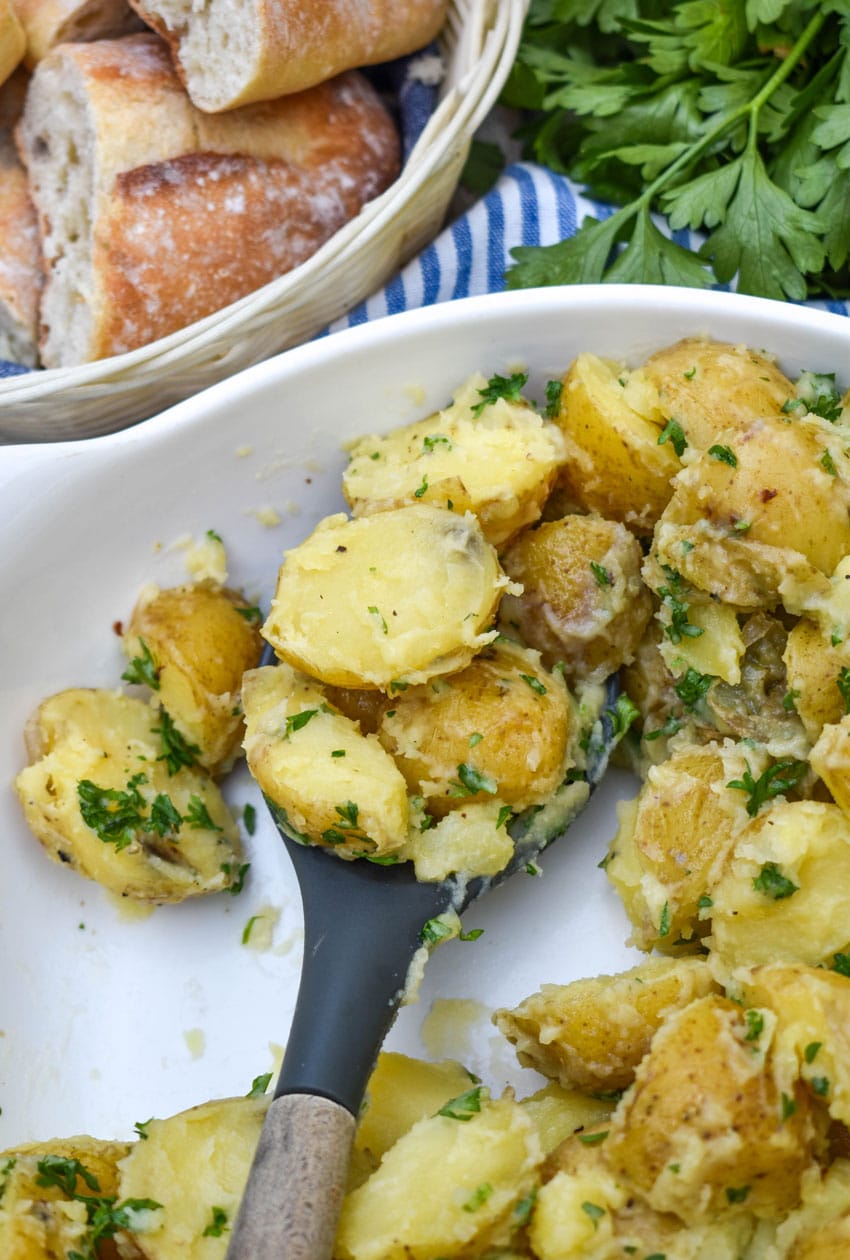 a serving spoon scooping butter and parsley potatoes out of a white serving bowl