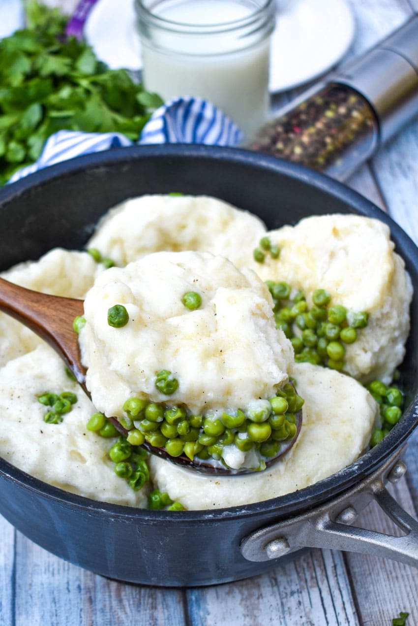 a wooden spoon scooping peas and dumplings out of a black pot