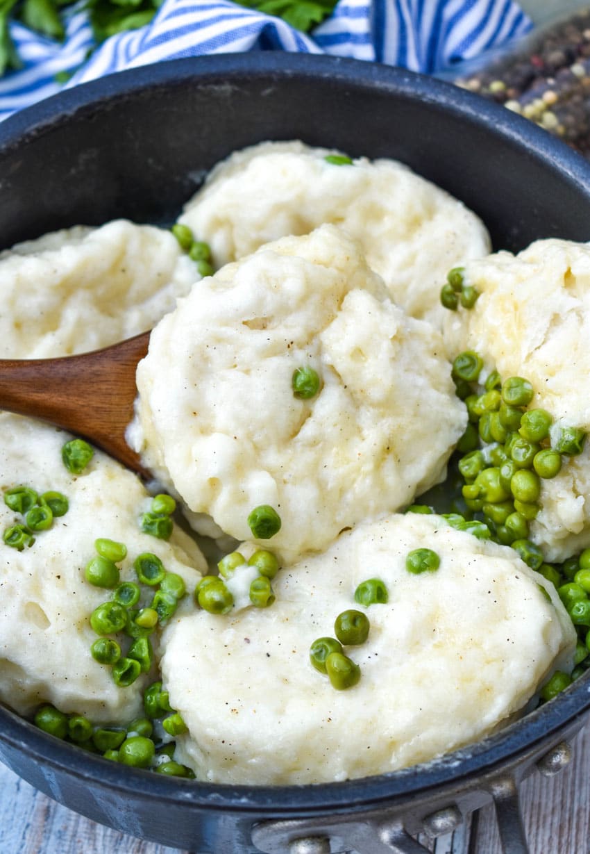 a wooden spoon scooping peas and dumplings out of a black pot