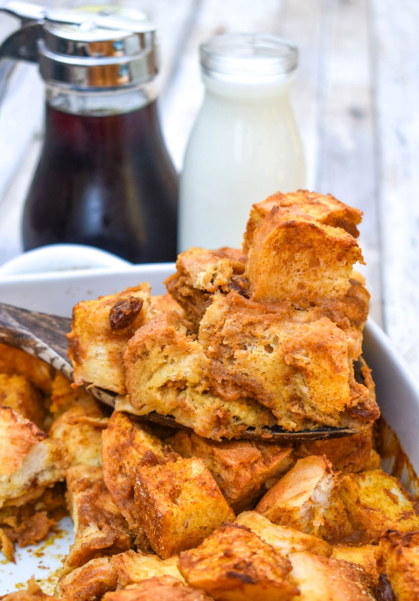 a wooden spatula lifting a slice of pumpkin bread pudding out of a white casserole dish
