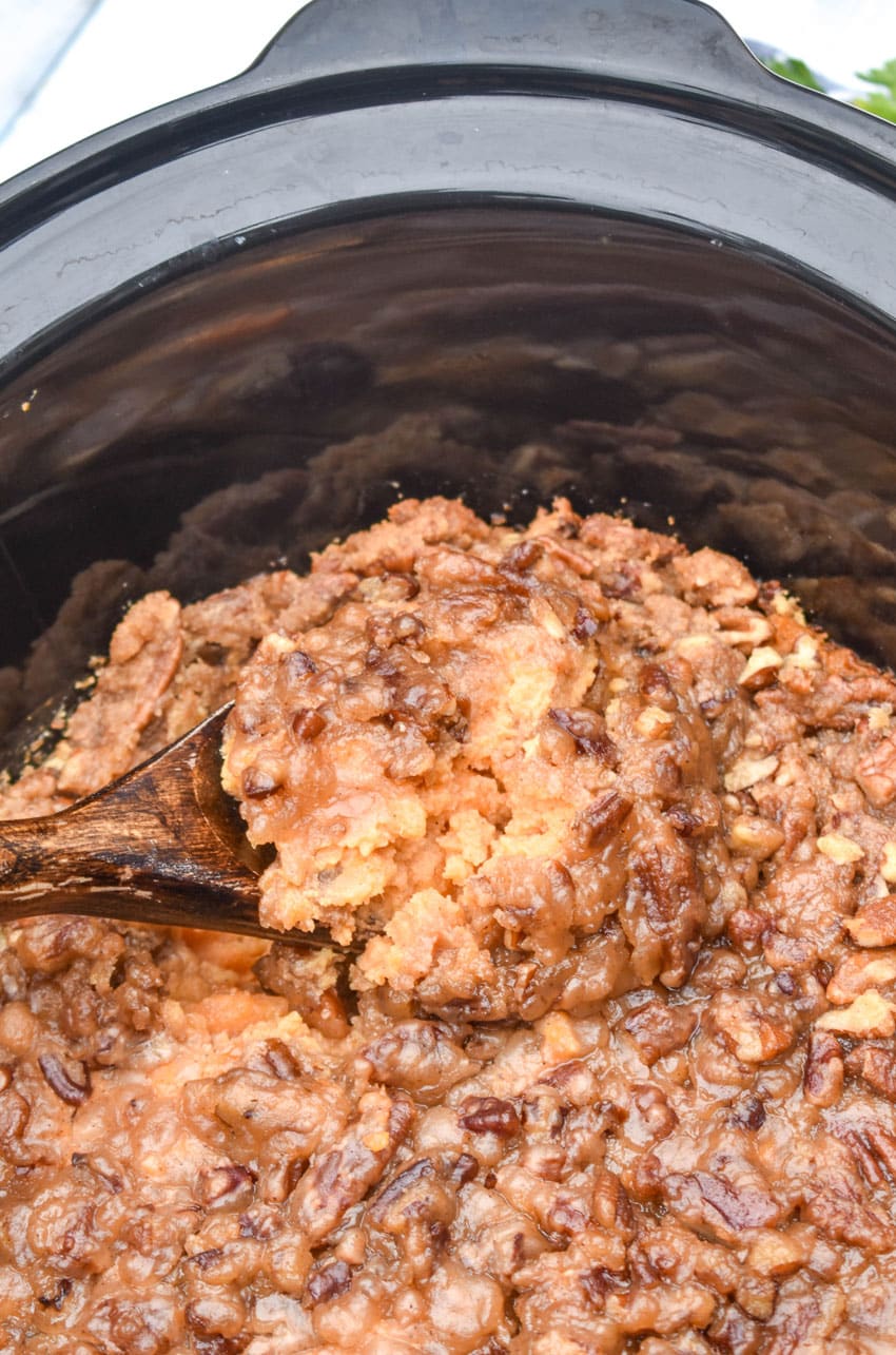 a wooden spoon scooping sweet potato casserole out of the black bowl of a slow cooker