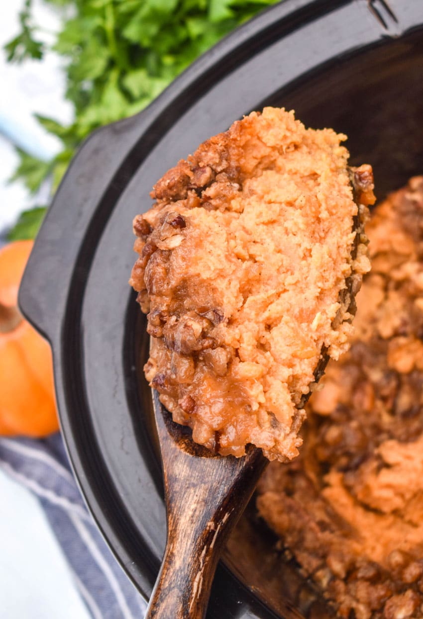a wooden spoon holding up a scoop of crockpot sweet potato casserole