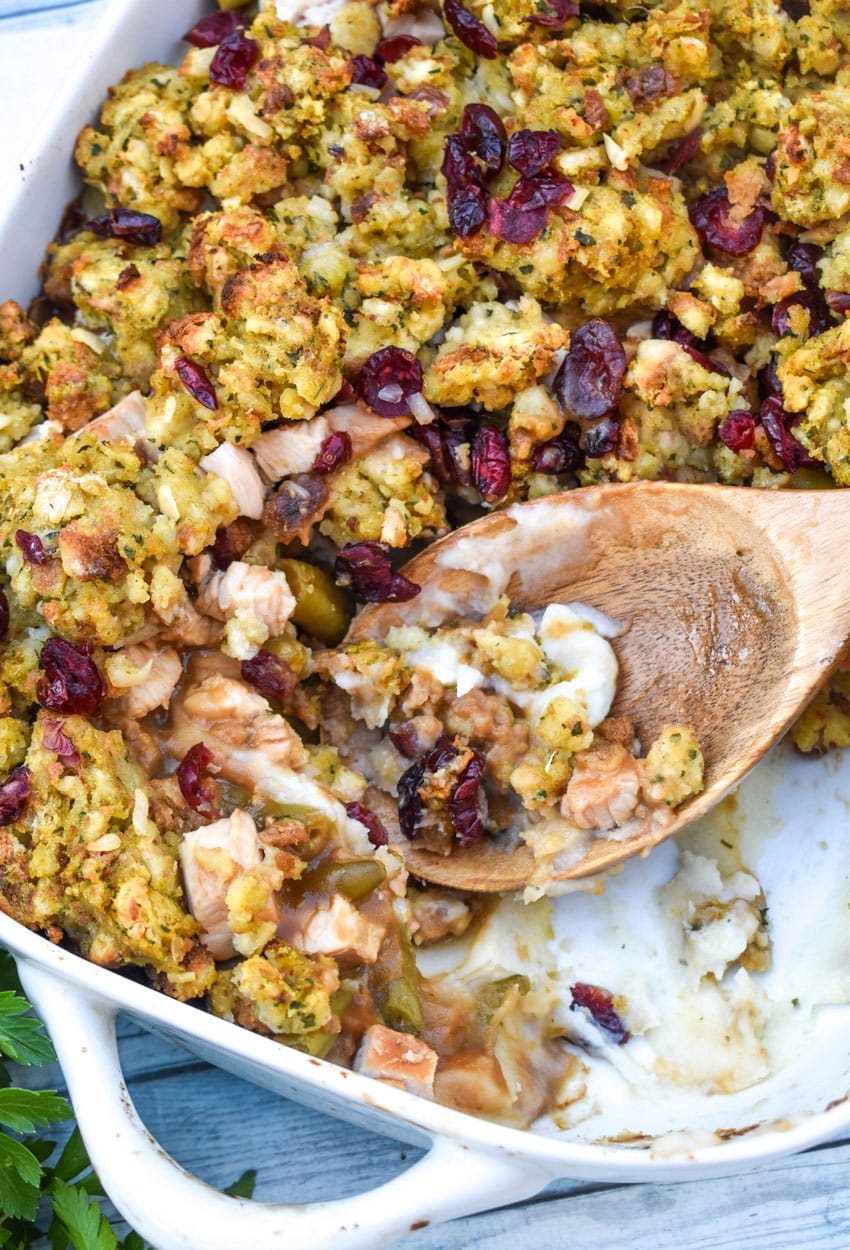 a wooden spoon scooping thanksgiving casserole out of a white baking dish